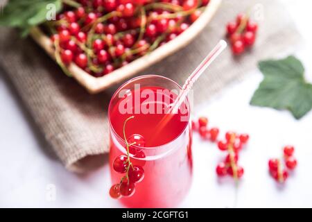 Zweige roter Johannisbeerenbeeren liegen in einer Weidenschale auf einem Sacktuch, eine Beerenmorse steht in einem Glas auf hellem Hintergrund. Sommerliche Getränke, die que Stockfoto