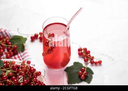 Zweige roter Johannisbeerenbeeren liegen in einer Weidenschale auf einem Sacktuch, eine Beerenmorse steht in einem Glas auf hellem Hintergrund. Sommerliche Getränke, die que Stockfoto