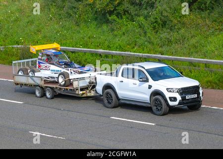 2020 weißer Ford Ranger Wildtrak ecoblue 4 Schleppen eines Stock-Rennwagens auf Anhänger; Fahrzeuge mit bewegtem Verkehr, Fahrzeuge, die Fahrzeuge auf britischen Straßen fahren, Motoren, Fahren auf dem Autobahnnetz der Autobahn M6. Stockfoto