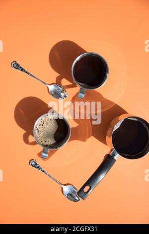 Ein sonniger Morgen, zwei Tassen Kaffee und eine Kanne Kaffee stehen auf einem orangefarbenen Hintergrund, die Sonne strahlt aus den Tassen. Vertikale Ausrichtung Stockfoto