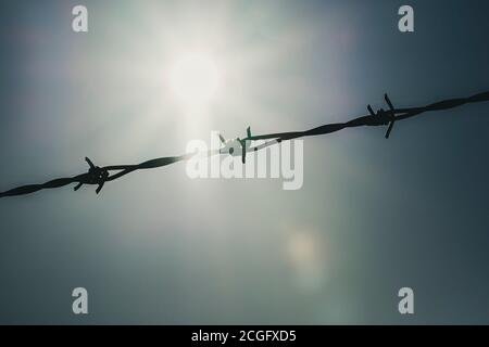Eine Länge von Stacheldraht an einem Wintermorgen in Silhouette agsint eine helle Sonne in ablue Himmel gesetzt. Stockfoto