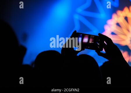 Leute, die einen DJ in einem Nachtclub aufnehmen und fotografieren, halten ihr Telefon über den Köpfen der Menge. Stockfoto