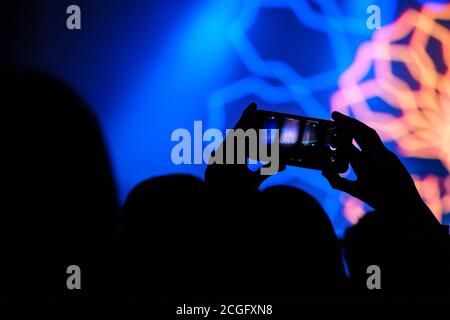 Leute, die einen DJ in einem Nachtclub aufnehmen und fotografieren, halten ihr Telefon über den Köpfen der Menge. Stockfoto