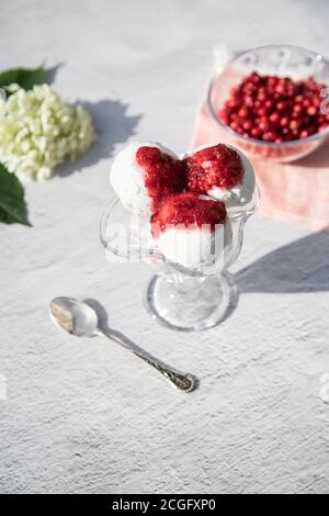 Glasschüssel mit Eiskugeln mit Preiselbeermarmelade auf hellem Hintergrund, Beeren in einer Glasschüssel. Vertikale Ausrichtung Stockfoto