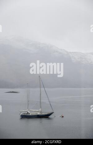 Eine kleine Yacht vertäut und verdeckt während eines Regensturms, während sie auf Loch Leven in Schottland schwimmt. Die Aussicht wird durch ein regnerisches Fenster verdeckt. Stockfoto