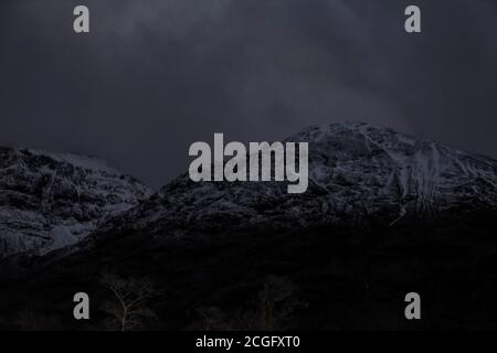 Schneebedeckte Berge in der Nacht, kaum gesehen durch den dunklen set aginsta wolkigen dunklen Himmel. Stockfoto