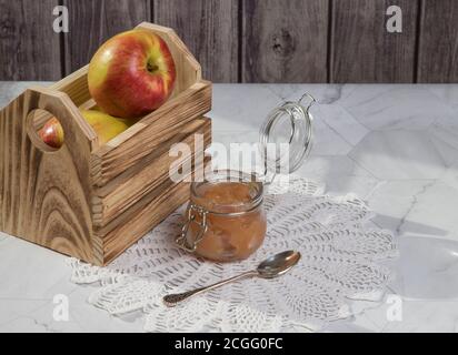 Ein Glas Apfelmus und Äpfel in einer Holzkiste auf hellem Hintergrund. Horizontale Ausrichtung Stockfoto