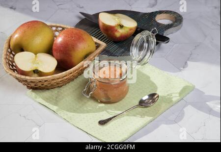 Eine Dose Apfelmus und Äpfel in einer Weidenplatte auf hellem Hintergrund, ein in Scheiben geschnittener Apfel auf einem Holzbrett. Horizontale Ausrichtung Stockfoto