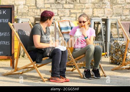 Lyme Regis, Dorset, Großbritannien. September 2020. Wetter in Großbritannien. Zwei Frauen sitzen in Liegestühlen mit einem frühen Mittagessen an der Küste im Badeort Lyme Regis in Dorset an einem Morgen von warmen nebligen Sonnenschein vor einer Mini-Hitzewelle nächste Woche. Bild: Graham Hunt/Alamy Live News Stockfoto