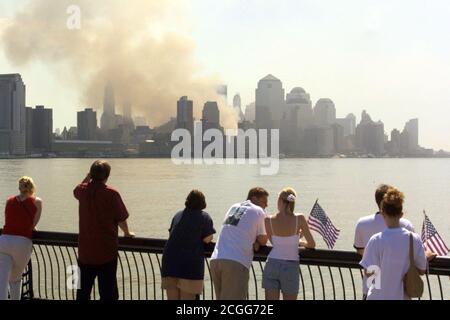 Menschen mit US-Flaggen blicken am 12. September 2001 von New Jersey aus auf die Skyline von Manhattan. Wo am Vortag die beiden Türme des World Trade Centers standen, ist nur eine Rauchwolke zu sehen. Am 11. September 2001 stürzten in schneller Folge zwei Flugzeuge in die Türme des World Trade Centers ein. Neben den Insassen der Maschinen wurden in den beiden Wolkenkratzern bei den schweren Explosionen zahlreiche Menschen getötet. Es wird angenommen, dass Tausende von Leichen unter den massiven Trümmerbergen des World Trade Centers liegen. Weltweite Nutzung Stockfoto