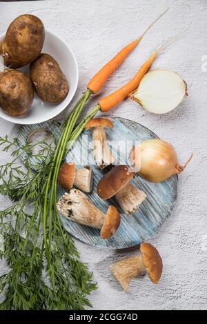 Zutaten zum Kochen Pilzsuppe-Steinpilze, Zwiebeln, Karotten, Kartoffeln auf hellem Hintergrund. Russische Küche. Vertikale Ausrichtung. Ort Stockfoto