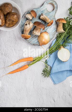 Zutaten zum Kochen Pilzsuppe-Steinpilze, Zwiebeln, Karotten, Kartoffeln auf hellem Hintergrund. Russische Küche. Vertikale Ausrichtung. Ort Stockfoto