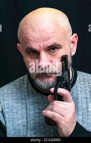 Kahlbärtiger Mann mittleren Alters mit einer Pistole in der Hand auf dunklem Hintergrund Stockfoto