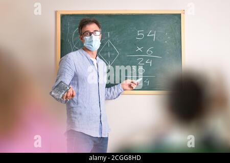 Mathematiklehrer in der Grundschule geschützt mit einer Maske fällig Risiko einer Coronavirus-Infektion erklären in der Klasse Stockfoto