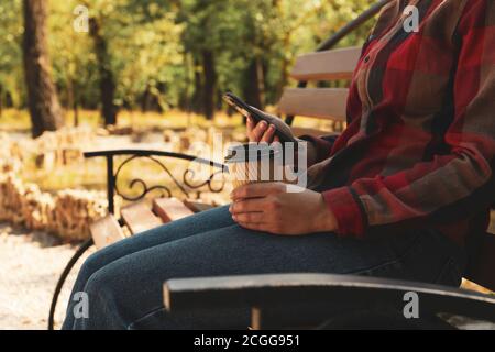 Frau in Jeans und Hemd halten Papierbecher und Telefon Im Freien Stockfoto