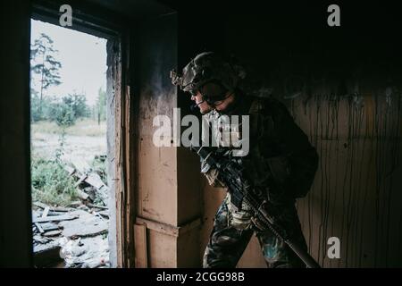 Soldat in voller US MARSOC bewaffnet mit Sturmgewehr durch das verlassene Gebäude laufen. Militärischer Zusammenstoß. Stockfoto