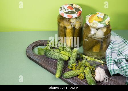 Eingelegte Gurken in Gläsern. Frische Gurken auf einem hölzernen Schneidebrett mit Knoblauch und Kräutern. Platz für den Kopierbereich. Horizontale Ausrichtung Stockfoto