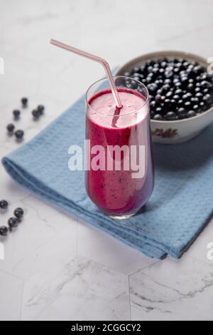 Die Diät trinken Heidelbeere Smoothie in einem Glas mit Stroh, weiße Platte mit Beeren auf hellem Hintergrund, mit einer blauen Serviette Stockfoto
