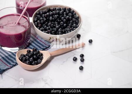 Auf einem hellen Hintergrund ist ein hoher Teller mit Heidelbeeren, zwei Gläser mit einer Diät Blaubeere Smoothie stehen auf einem hellen Hintergrund, ein Holzlöffel mit Be Stockfoto