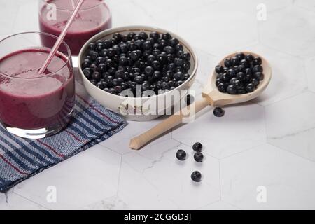 Auf einem hellen Hintergrund ist ein hoher Teller mit Heidelbeeren, zwei Gläser mit einer Diät Blaubeere Smoothie stehen auf einem hellen Hintergrund, ein Holzlöffel mit Be Stockfoto