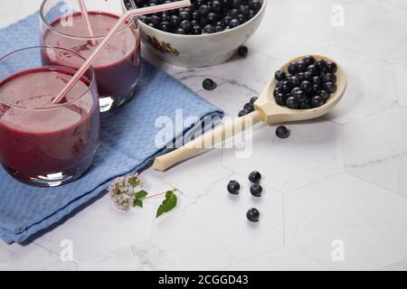 Auf einem hellen Hintergrund ist ein hoher Teller mit Heidelbeeren, zwei Gläser mit einer Diät Blaubeere Smoothie stehen auf einem hellen Hintergrund, ein Holzlöffel mit Be Stockfoto