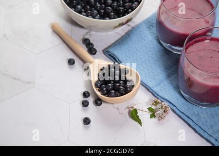 Auf einem hellen Hintergrund ist ein Holzlöffel mit Heidelbeeren, zwei Gläser mit einer Diät Heidelbeere Smoothie sind auf einer blauen Serviette. Platz für den Kopierbereich Stockfoto