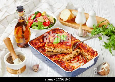Lasagne auf pflanzlicher Basis mit Tofu, Pilzen, Passata-Sauce in einer Backform serviert mit einem frischen Salat aus Salat, Tomaten, Gurke, rote Zwiebel und Basilikum l Stockfoto