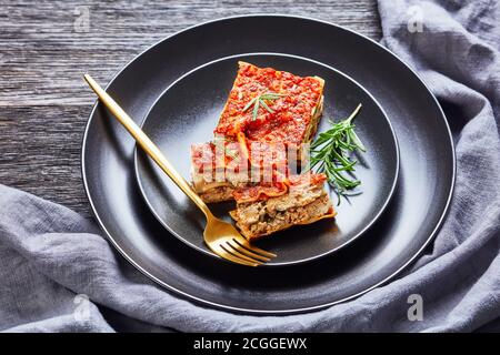 Vegane Tofu Spinatlasagne mit Champignon und Tomaten vegane Bolognese Und italienische Würze serviert auf einem schwarzen Teller mit Gabel Und frischen Rosmarin auf einem Stockfoto