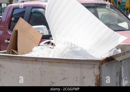 Überlaufender Mülleimer auf einer Stadtstraße vor einem Auto. Plastikmüll im Papierkorb Stockfoto