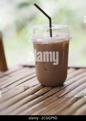 Nahaufnahme von Eiswürfeln in kaltgebrühtem Kaffee Cappuccino in Plastikbecher auf Bambus-Holztisch gestellt verschwommener Hintergrund, Getränk trinken Stockfoto