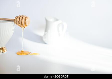 Honig fließt aus gedrehtem Honigstock. Honigs tun auf weißem Hintergrund. Frühstücksahnekännchen Stockfoto