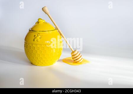 Gelbes Fass mit Honig neben dem hölzernen Honigriegel. Honigstock mit fließendem Honig auf weißem Hintergrund. Für Text platzieren Stockfoto