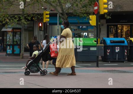 Zaragoza, Spanien - 18. August 2020: Eine schwarze Inmigrantin, mit Gesichtsmasken, wegen der Coronavirus-Pandemie, schiebt einen Kinderwagen mit ihrem Kind in den Stockfoto
