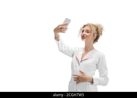 Selfie-Zeit. Porträt einer Ärztin, Krankenschwester oder Kosmetologin in weißer Uniform und blauen Handschuhen auf weißem Studiohintergrund. Copyspace für Werbung. Konzept von Gesundheit und Medizin, Schönheit, Selbstversorgung. Stockfoto