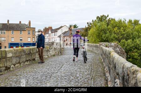 Älterer Mann mit Gesichtsmaske und Frau schieben Fahrrad soziale Distanzierung auf Roman Bridge, Musselburgh, East Lothian, Schottland, Großbritannien Stockfoto