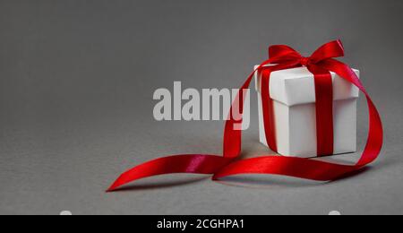 Weihnachtsgeschenk in weißer Schachtel mit rotem Band auf dunkelgrauem Hintergrund. Neujahrsfeiertag – Composition Banner. Platz Für Ihren Text Kopieren Stockfoto