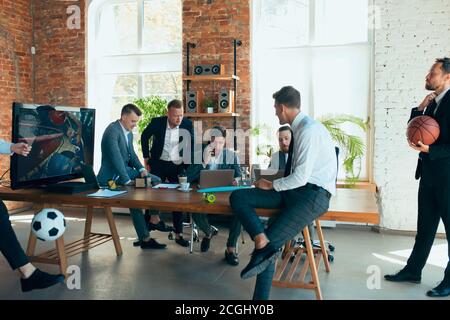 Spielen von Basketball, Videospielen, Fußball. Glückliche, unbeschwerte Kollegen, die Spaß im Büro haben, während ihre Kollegen hart und hochkonzentriert arbeiten. Konzept von Spaß, Ruhe, Beruf. Stockfoto