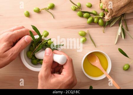 Person Hände Herstellung Olivenöl Essenz mit Mörser für Körper und kulinarische Pflege auf dem Tisch mit Sack Oliven. Draufsicht. Stockfoto