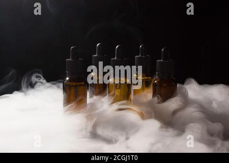 Glasflaschen mit Pipetten und VAPE-Flüssigkeit. Dicker Dampf vom Rauchen einer elektronischen Zigarette. Stockfoto