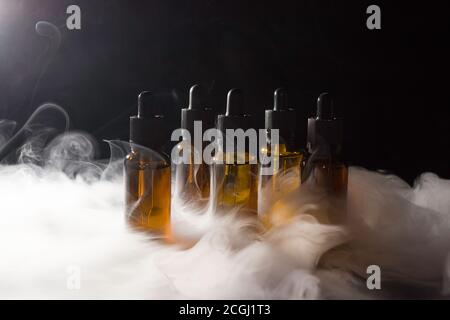 Glasflaschen mit Pipetten und VAPE-Flüssigkeit. Dicker Dampf vom Rauchen einer elektronischen Zigarette. Stockfoto