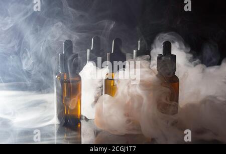 Glasflaschen mit Pipetten und VAPE-Flüssigkeit. Dicker Dampf vom Rauchen einer elektronischen Zigarette. Stockfoto