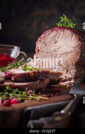 Gebackenes Schweinefleisch mit Preiselbeersoße und Thymian über Holz- Hintergrund. Konzepte von Essen. Stockfoto