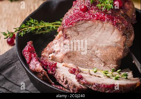 Gebackenes Schweinefleisch mit Preiselbeersoße und Thymian über Holz- Hintergrund. Konzepte von Essen. Stockfoto