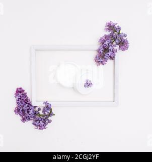 Creme in einem Glas in einem hölzernen weißen Rahmen auf weißem Hintergrund und lila Blumen. Konzept der Hautpflege, Spa. Stockfoto