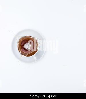 Ein Zuckerwürfel fällt in eine weiße Tasse Tee und spritzt. Draufsicht, weißer Hintergrund, freier Platz für Text. Stockfoto