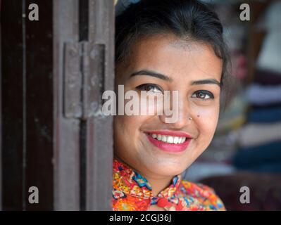 Attraktive junge Nepalesin gucken um eine alte Holztür und lächeln für die Kamera. Stockfoto