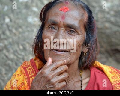 Die alte nepalesische Bettlerin und Hindu-Anhängerin mit roter Reistilak-Markierung auf ihrer Stirn berührt ihr Kinn. Stockfoto