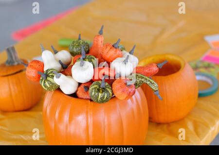 Das horizontale Foto eines dekorativen Bouquets der Kürbisse Im orangefarbenen Eimer auf dem mit einer Oreange bedeckten Tisch Tischtuch Stockfoto