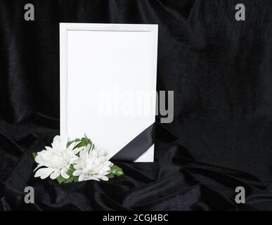 Kondolenzkarte. Gedenkrahmen mit schwarzem Band. Weiße Blüten. Schwarzer Hintergrund. Stockfoto