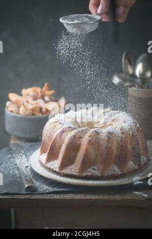 Landhausstil Apple Bundt Cake bestreut mit Puderzucker auf alten Holztisch mit Frau Hände Stockfoto